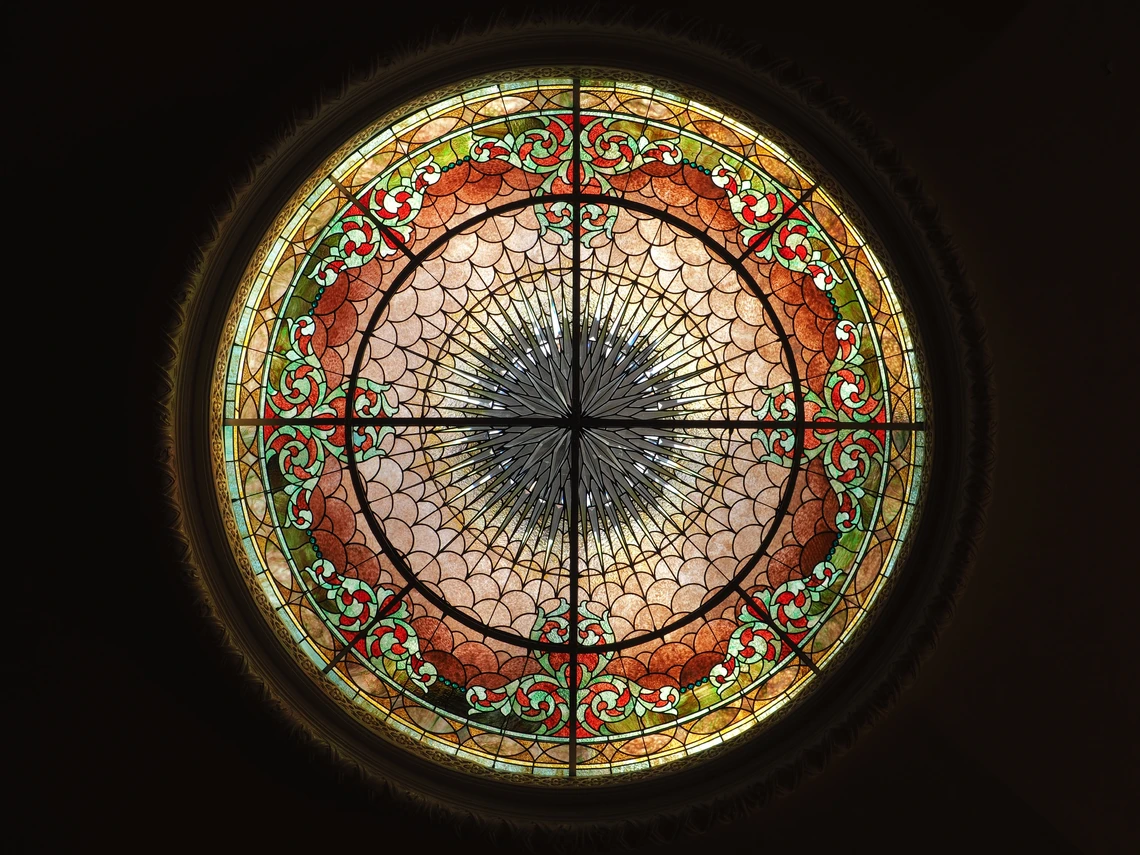 A large circular stained-glass window features light green, rust, gold, and light pink decorative scrolling and scalloped patterns.