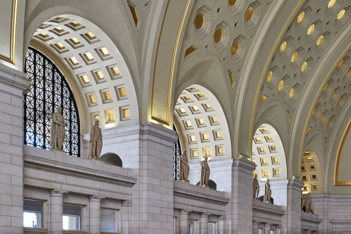 The interior of a grand interior space features a large vaulted ceiling, stone statues, and gilded decorations.