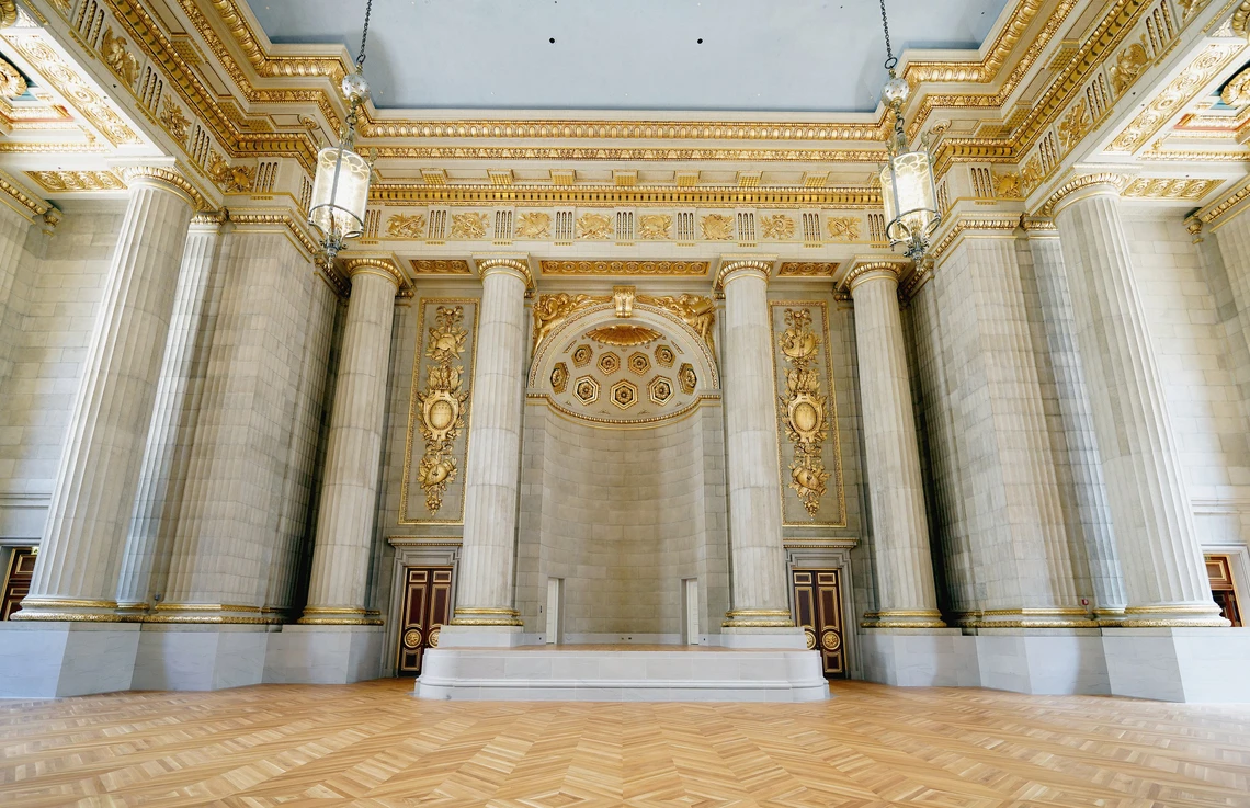 This image shows the interior of a large, intricately decorated room with columns, capitals, and gilded moldings.
