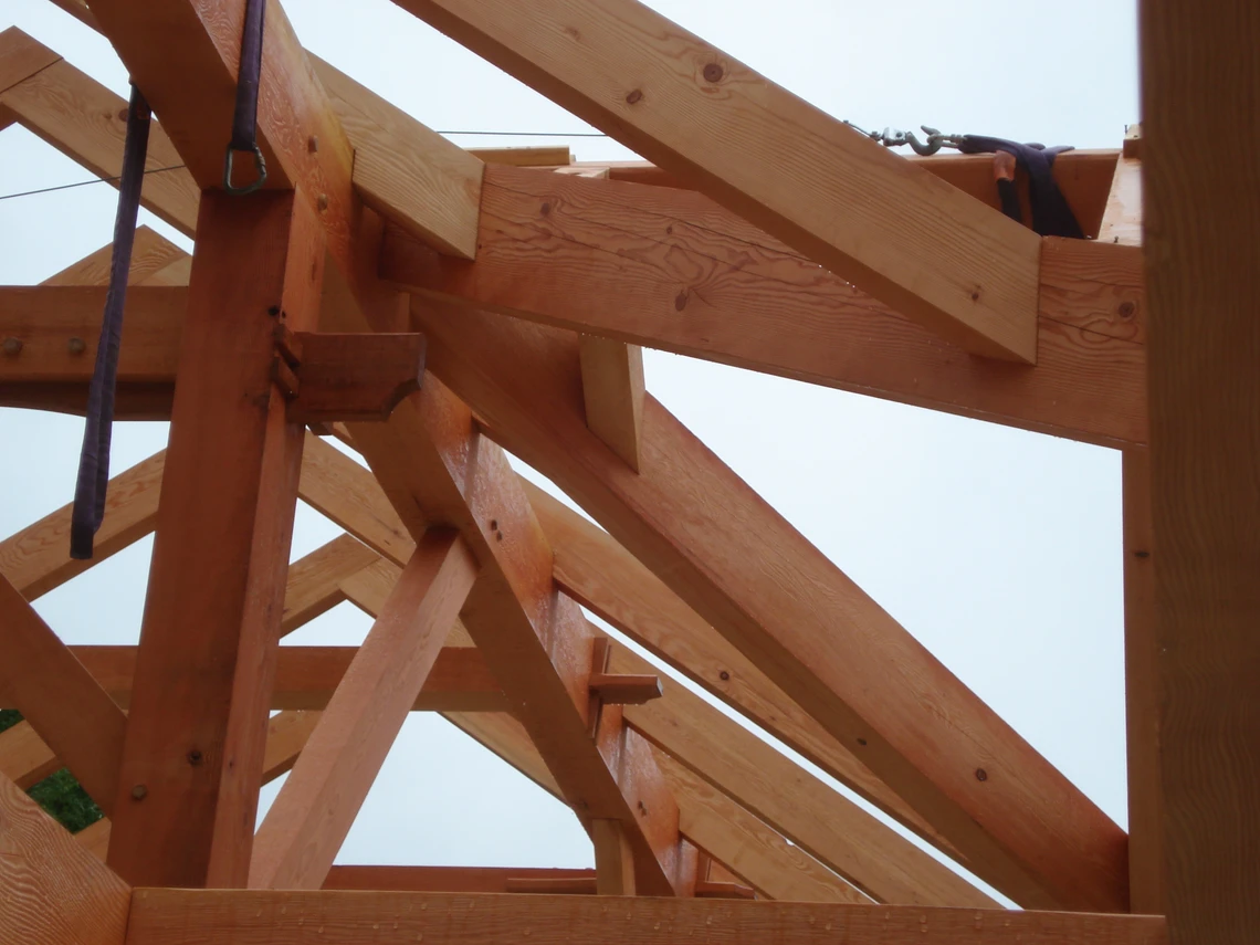 This image shows a close-up of several large crisscrossing rectangular wooden beams that form the roof of a timber-frame building.