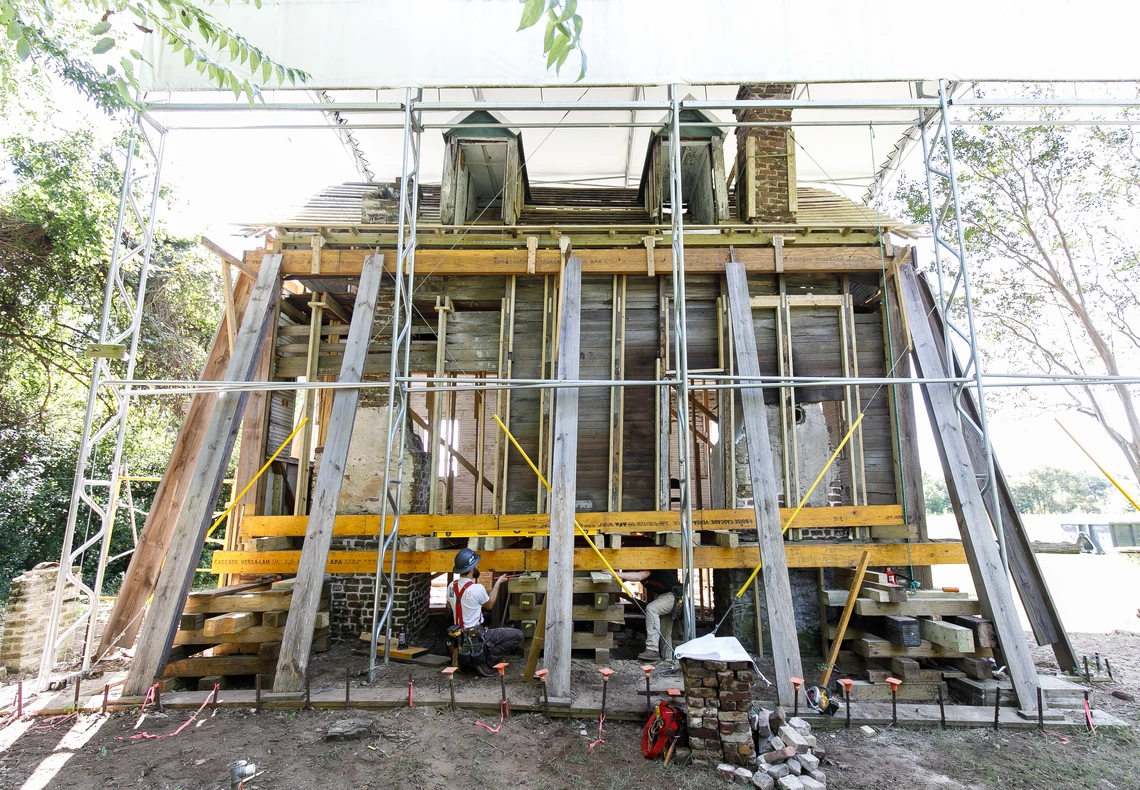 An old, damaged wooden house is covered in scaffolding and sturdy stabilization beams.
