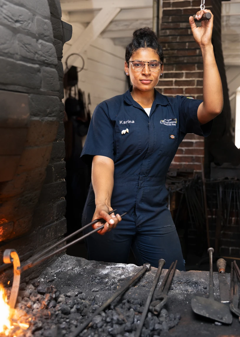 A young woman proudly poses at a coal-fired forge.
