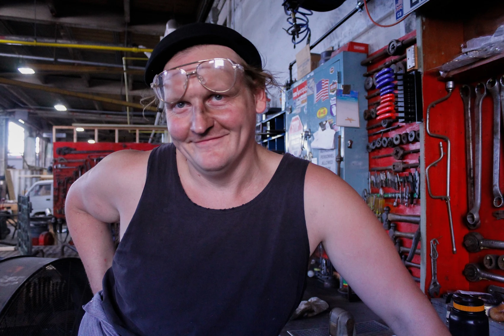A man with glasses on top of his head and a smile on his face poses in a blacksmith’s shop.