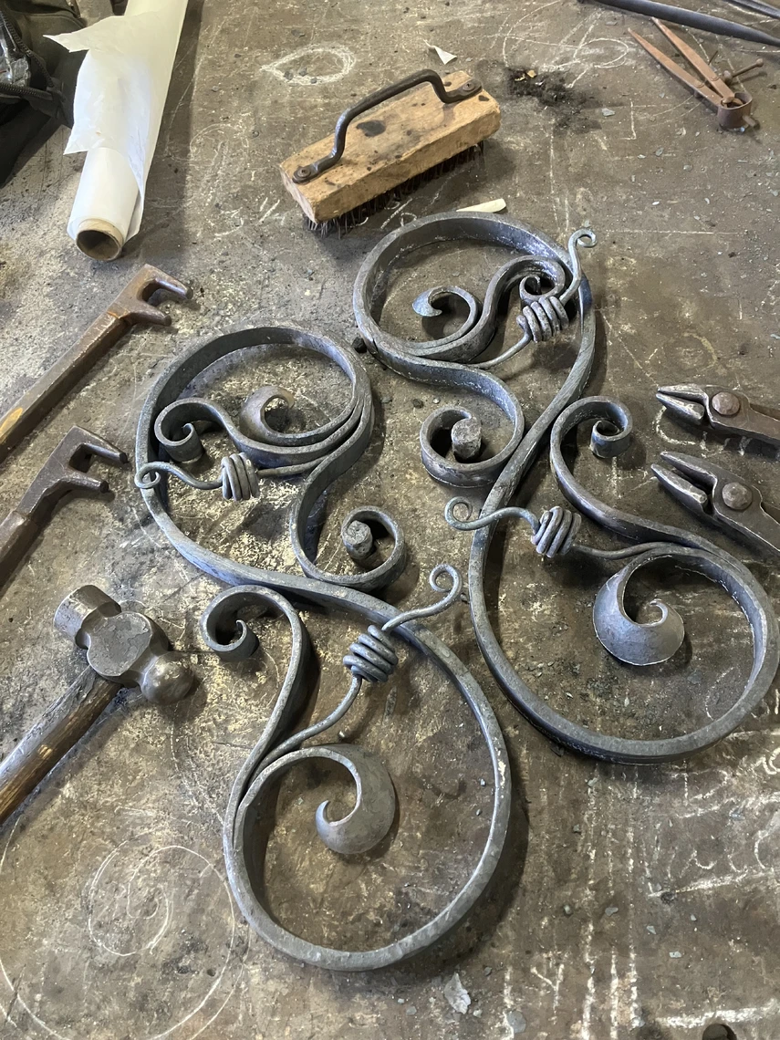 Two decorative hand-forged metal scrolls are displayed on a worktable in a blacksmith shop.