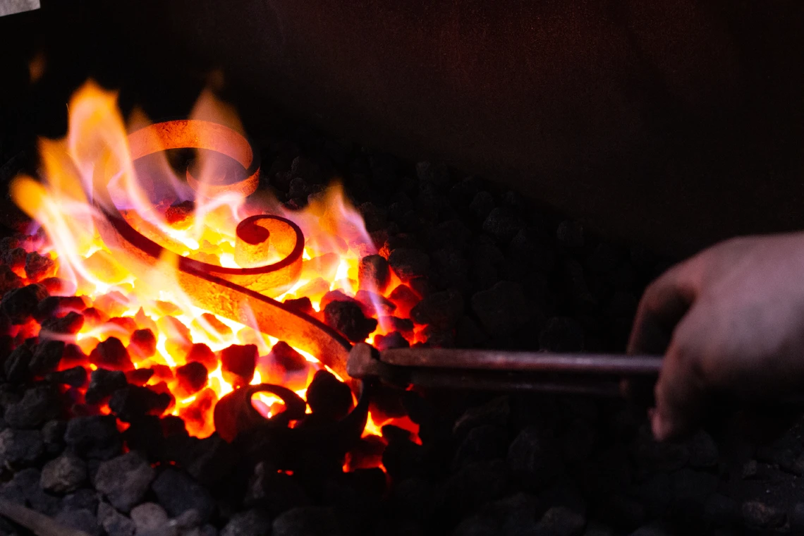 A red-hot piece of metal scrollwork is nestled in the orange flames of a fire in a blacksmith’s forge.