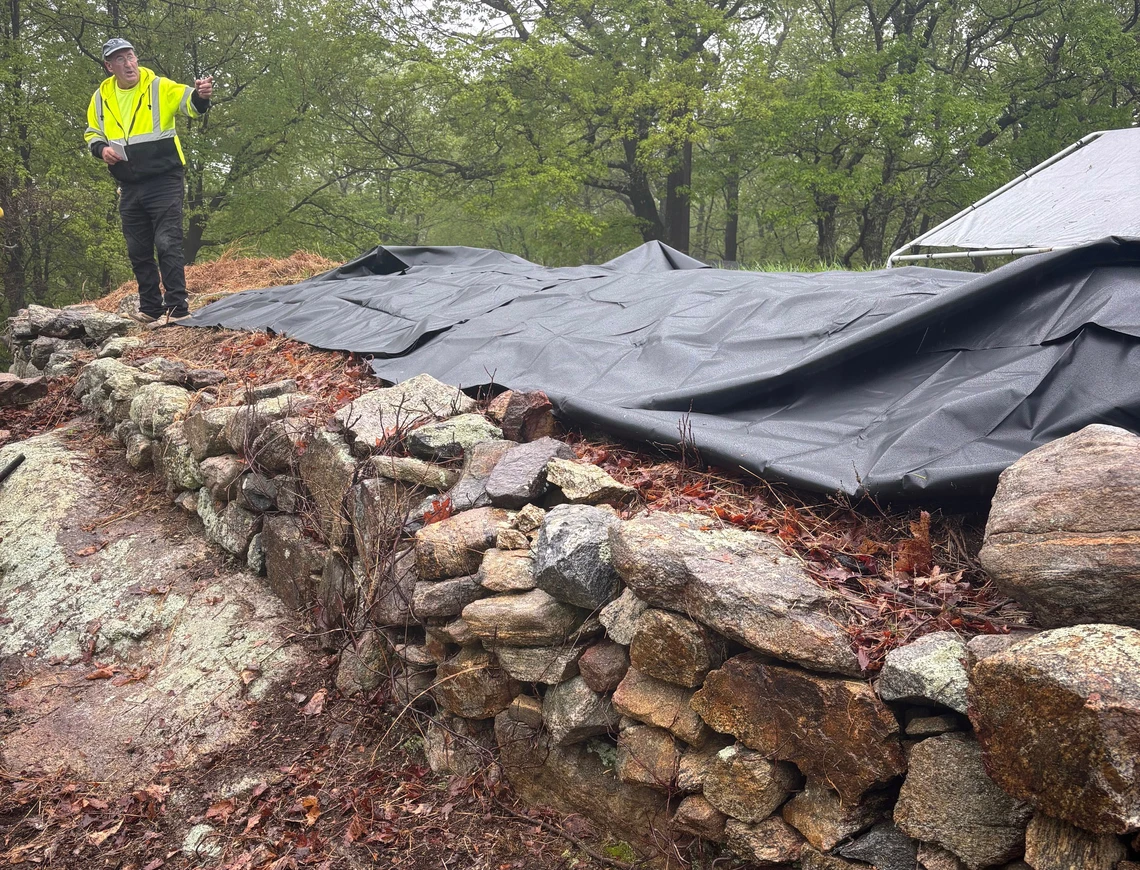 A man stands on an old, crumbling drystone wall in need of repair.