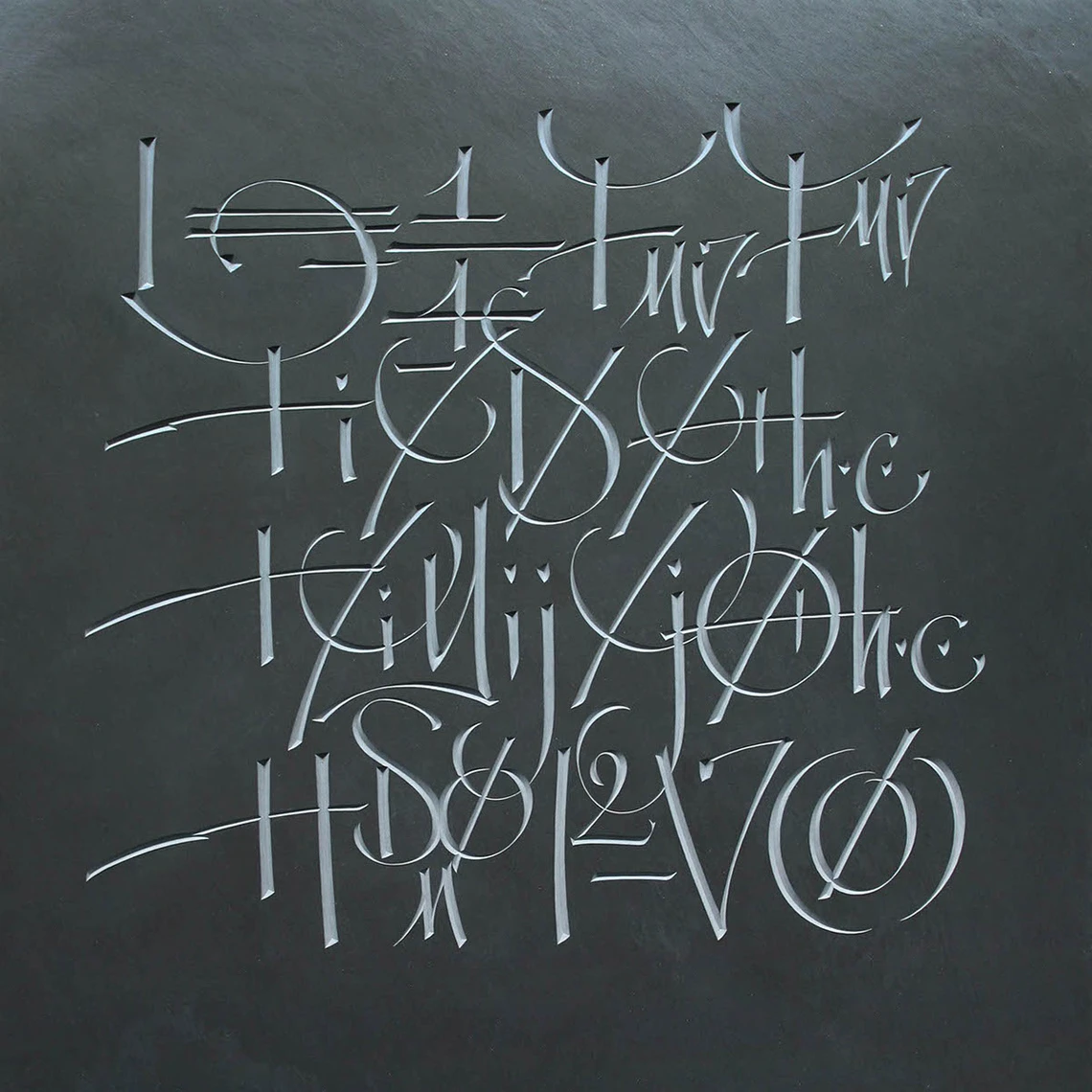 A square piece of dark-grey slate features abstract hand-carved symbols.