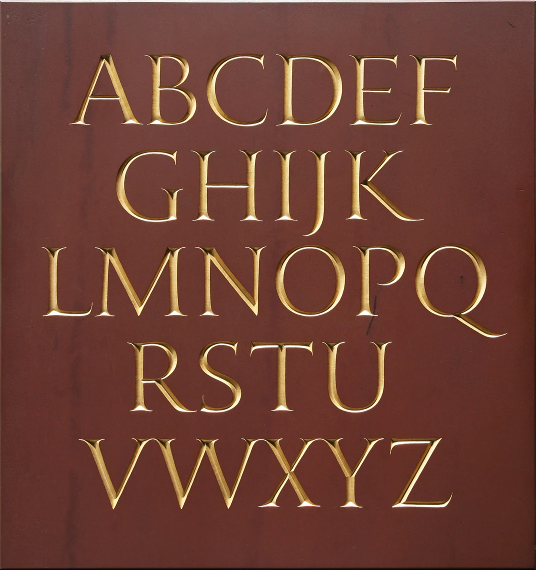 A square tablet of stone features the carved gold-stained capital letters of the alphabet.