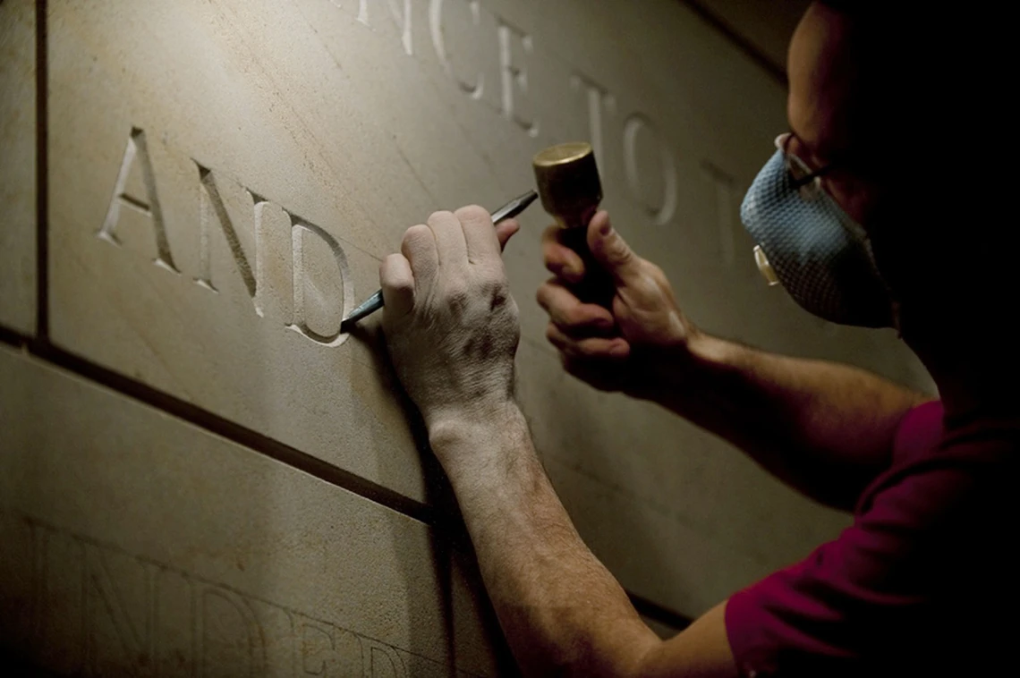 A man carves letters in stone with a hammer and chisel.