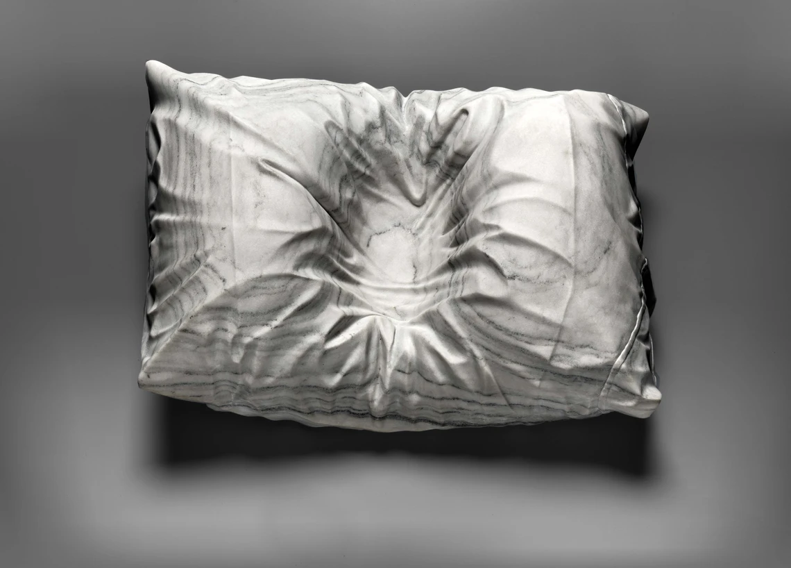 An image of a carved marble pillow with the indentation of a person’s head in the middle of the pillow.