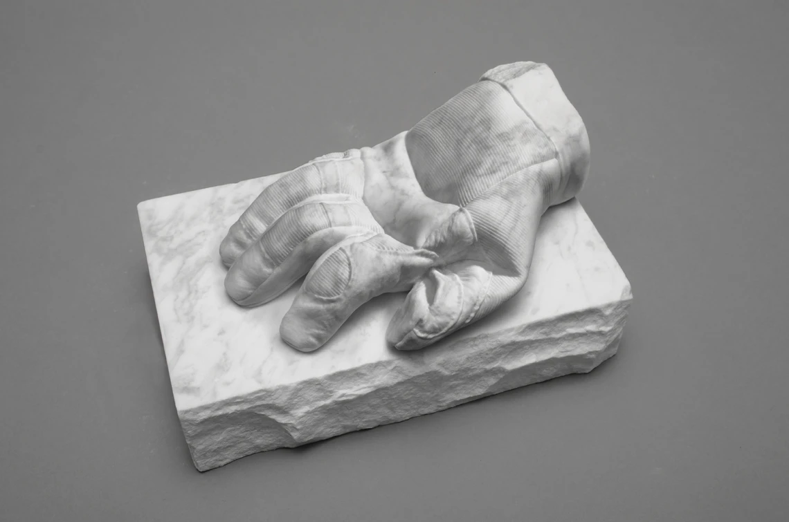 An image of a carved marble worker’s glove resting on top of a carved piece of stone.