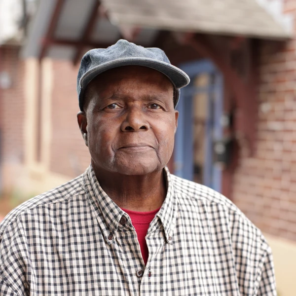 A man proudly poses in front of a brick building.